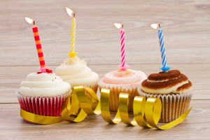 four birthday cupcakes with burning candles on wooden table